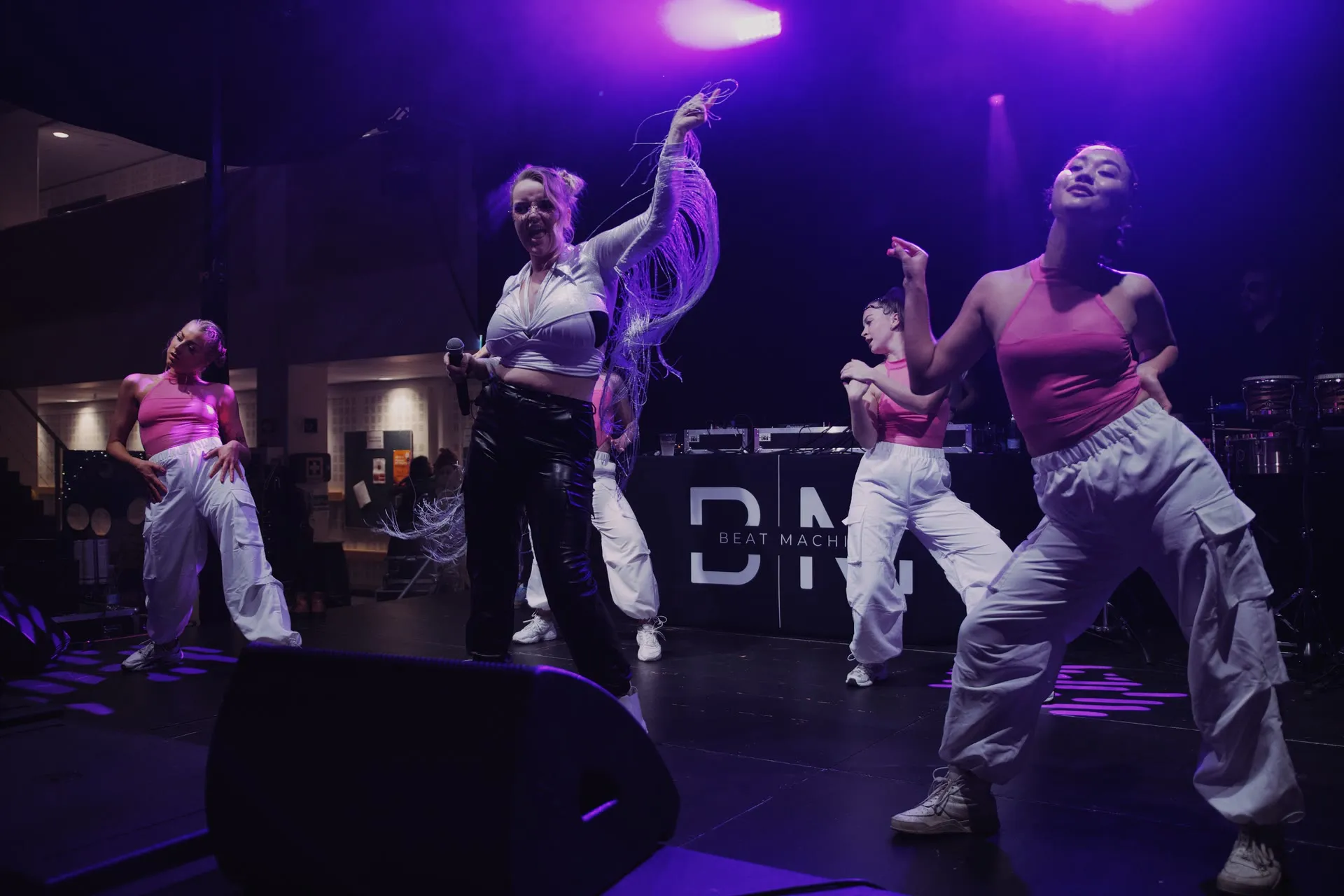 Beat Machine dansere i pink toppe og lilla scenelys